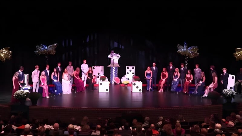 Schüler der Rockford High School treten in farbenfrohen Kostümen mit aufwendigen Kopfschmuck auf einer Bühne mit dekorativem Hintergrund auf.