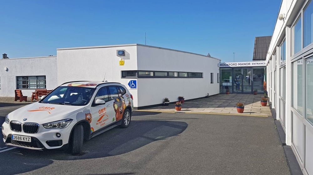 Ein weißer BMW X1 steht vor dem Haupteingang des Gebäudes der Rockford Manor School.
