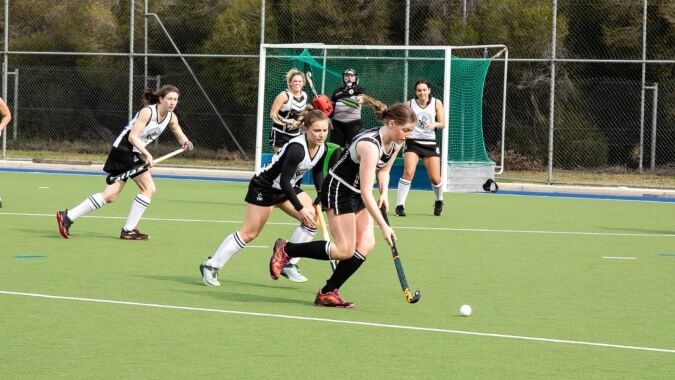 Schüler der Rockford Manor School spielen ein Feldhockeyspiel auf einem Kunstrasenplatz im Freien.
