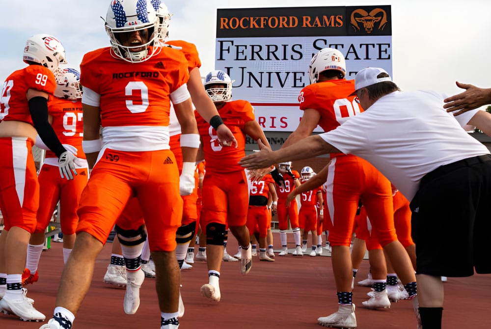 Eine Gruppe von Footballspielern in orangefarbenen Trikots steht auf dem Spielfeld der Rockford High School.