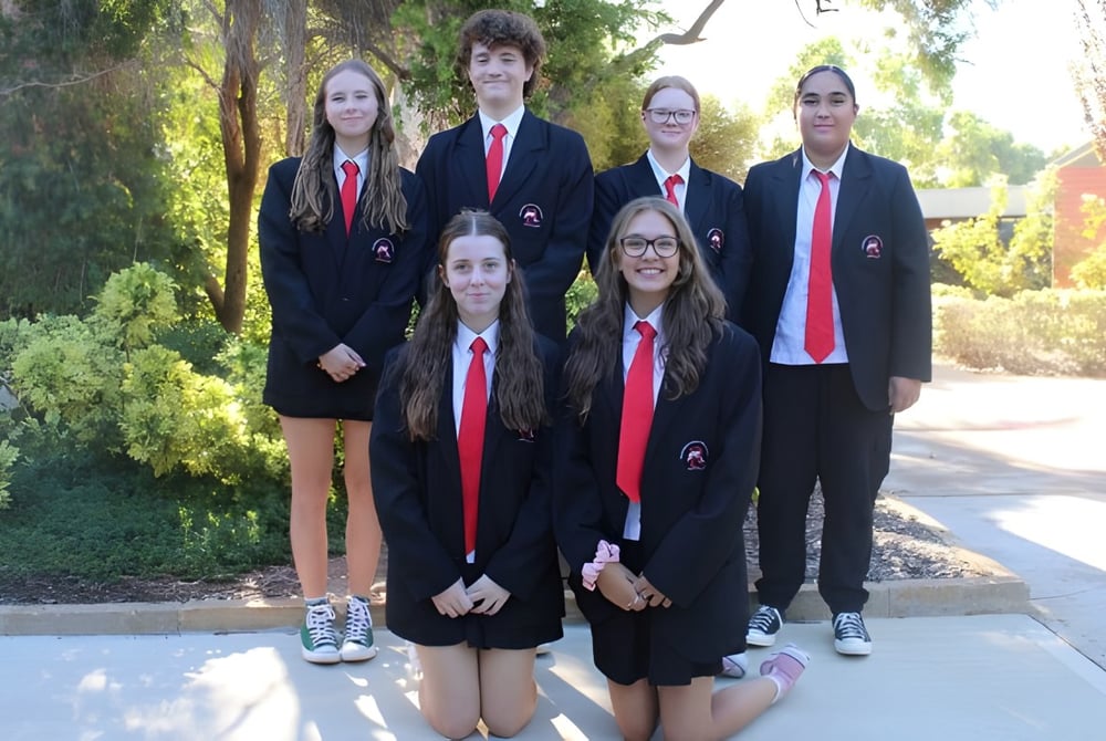 Eine Gruppe von sechs Schülern der Rockingham Senior High School steht in formeller Kleidung im grünen Außenbereich der Schule.