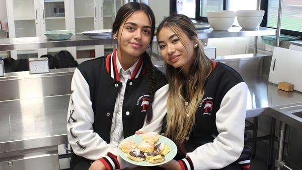 Zwei Schülerinnen der Rockingham Senior High School stehen in einer Küche und halten einen Teller mit Gebäck.