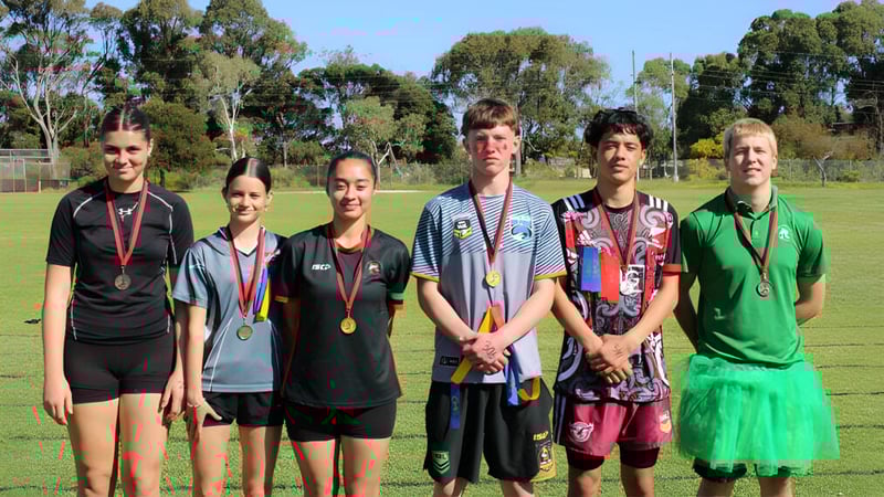 Eine Gruppe von jungen Athleten der Rockingham Senior High School steht auf einem grasbewachsenen Spielfeld unter blauem Himmel.