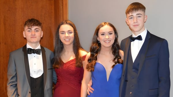 Vier Schülerinnen und Schüler der Rockport School posieren in formeller Kleidung vor einem Holzhintergrund.