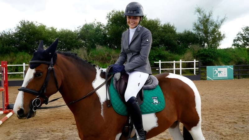 Eine Person in Reitausrüstung reitet ein braunes Pferd in der Außenanlage der Rockport School.