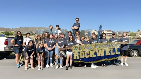 Eine Gruppe junger Menschen posiert vor einem Rockwell Charter School Banner mit Berglandschaft im Hintergrund.