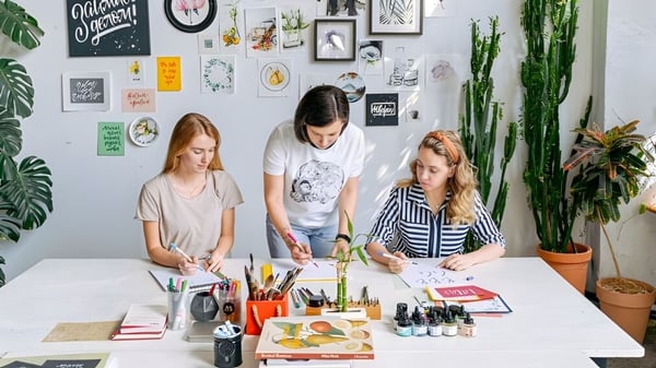 Drei Schüler der Rockwell Charter School sitzen an einem Tisch und arbeiten im Kreativunterricht an Zeichnungen und Malereien.