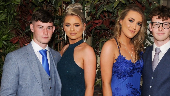 Vier Personen in formeller Kleidung stehen vor tropischer Vegetation auf dem Gelände des Rockwell College.