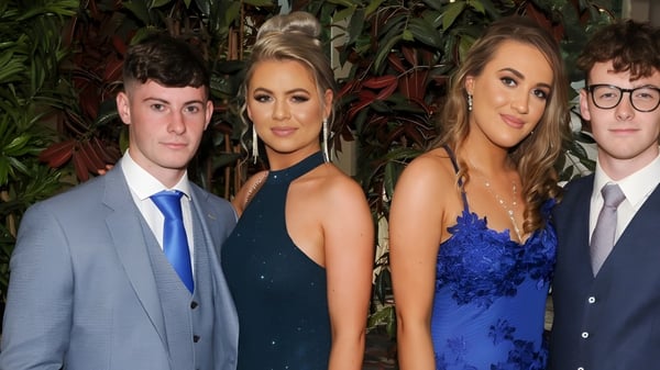 Vier Personen in formeller Kleidung stehen vor tropischem Grün auf dem Campus des Rockwell College.