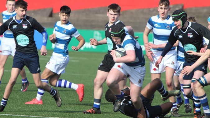 Eine Gruppe Rugbyspieler der Rockwell College trägt Uniform und spielt ein intensives Match auf einem Rasenfeld.