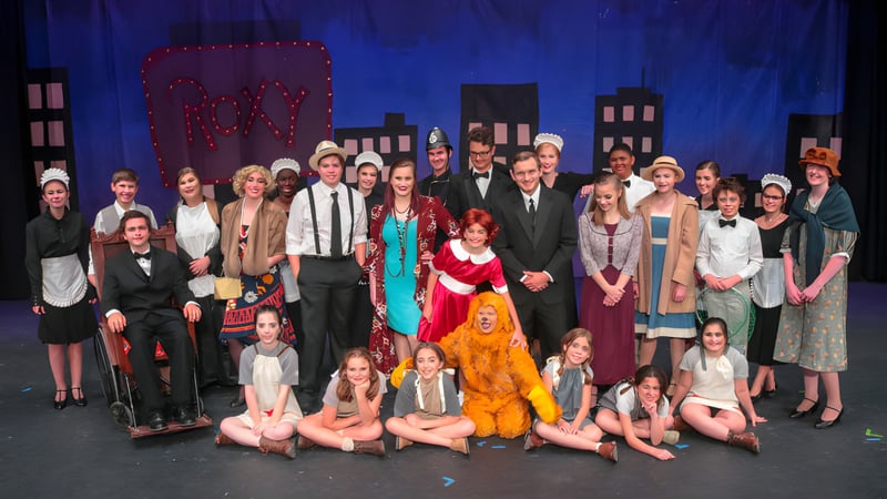 Eine große Gruppe Schüler der Rocky Bayou Christian High School posiert in Kostümen und formeller Kleidung auf einer Bühne mit blauem Hintergrund.