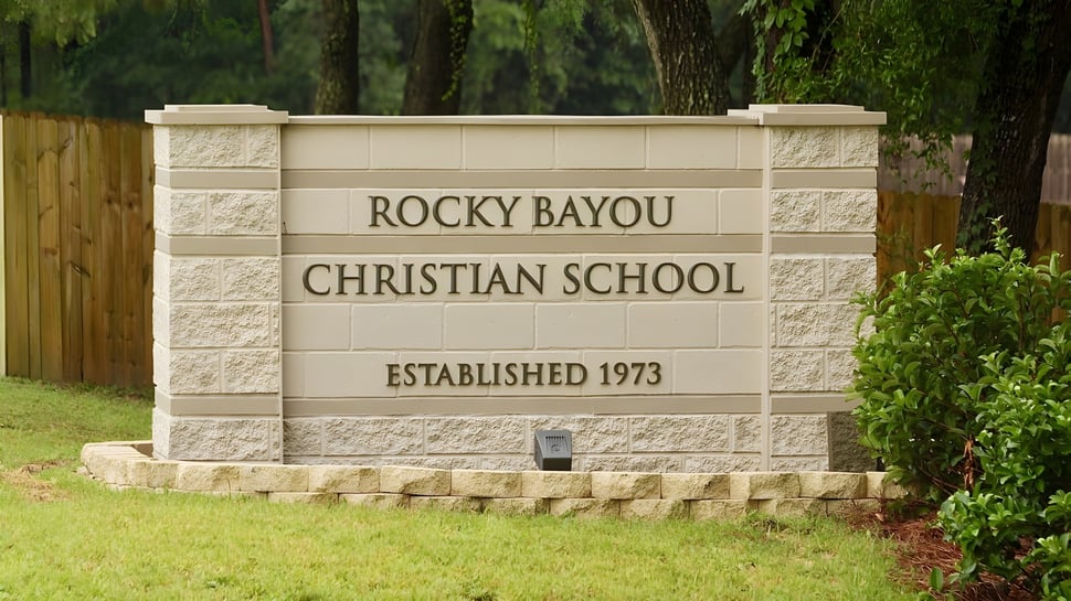 Das Steinschild zeigt den Namen Rocky Bayou Christian High School und das Gründungsjahr 1973 vor grünem Laubwerk.