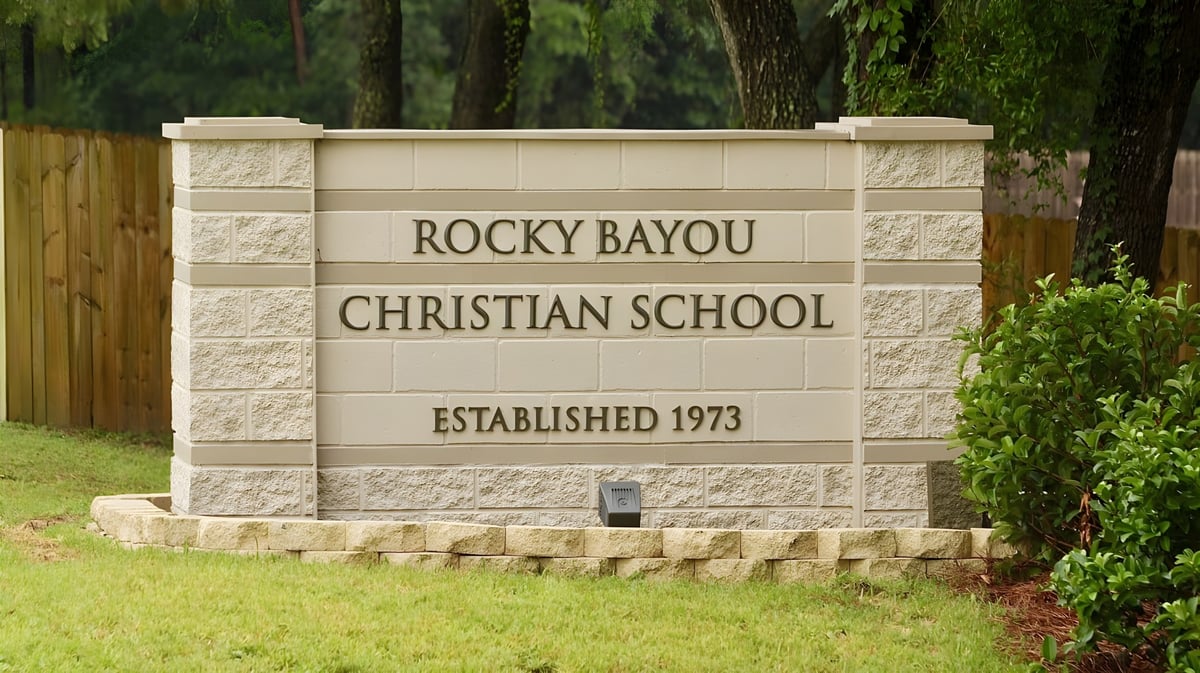 Das Steinschild zeigt den Namen Rocky Bayou Christian High School und das Gründungsjahr 1973 vor grünem Laubwerk.