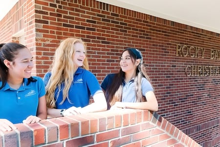Drei Schülerinnen der Rocky Bayou Christian High School stehen gemeinsam vor einer Backsteinmauer.