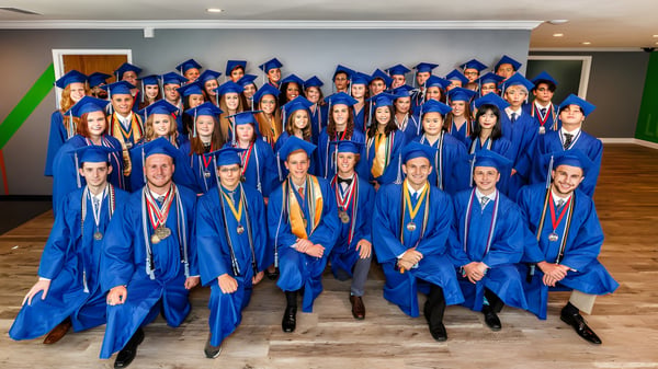 Eine große Gruppe von Absolventinnen und Absolventen in blauen Talaren steht im Raum der Rocky Bayou Christian High School.