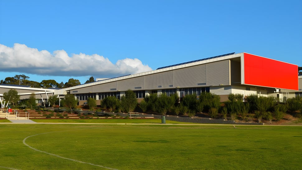 Das moderne Hauptgebäude des Roma Mitchell Secondary College steht vor einer Wiese mit Bäumen unter blauem Himmel.
