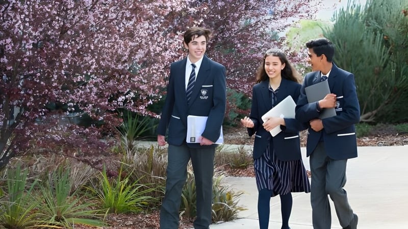 Drei Personen stehen zusammen im Garten vor blühenden Kirschblüten auf dem Gelände der Roma Mitchell Secondary College.