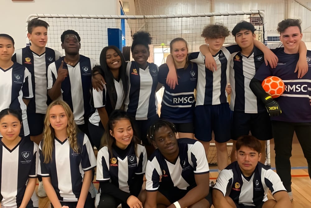 Eine Gruppe von Schülerinnen und Schülern des Roma Mitchell Secondary College posiert gemeinsam in einer Sporthalle mit Volleyballnetz im Hintergrund.