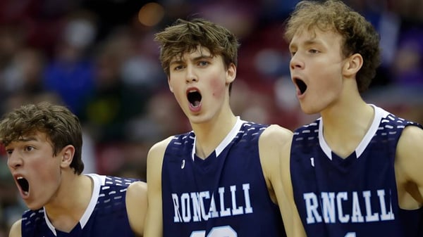 Drei Schüler der Roncalli Catholic High School in Basketballuniform beim Spiel mit intensiven Gesichtsausdrücken.