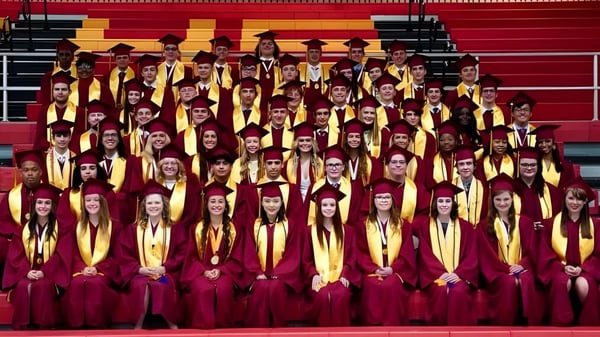Schüler der Roncalli Catholic High School stehen in roten und goldenen Roben gemeinsam auf einer Bühne bei der Abschlussfeier.