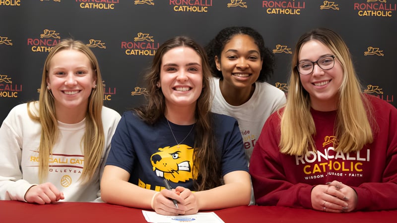 Vier Schülerinnen posieren gemeinsam vor einem Roncalli Catholic High School Logo.