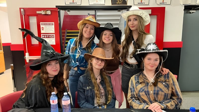 Eine Gruppe Schülerinnen der Roncalli Central High trägt verschiedene Hüte und Kostüme in einem Raum mit Schließfächern.