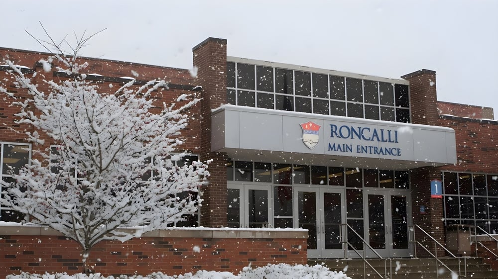 Ein schneebedeckter Baum steht vor dem Backsteingebäude mit dem Haupteingang der Roncalli Central High.