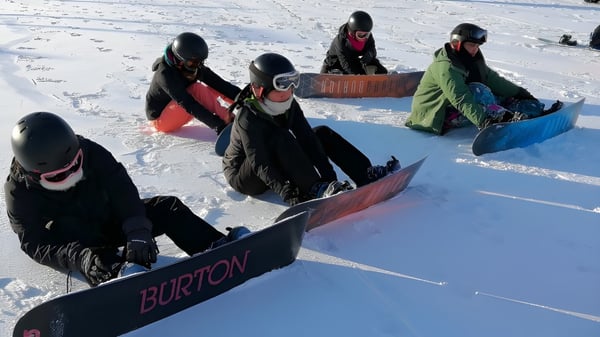 Schüler des Roncalli College tragen auf dem verschneiten Hang Snowboards und bereiten sich auf das Snowboarden vor.