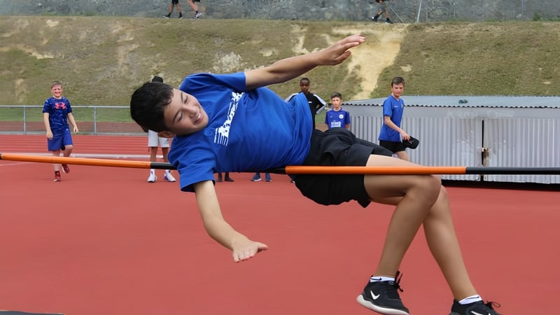 Ein Schüler des Rongotai College führt auf einer roten Fläche eine Gymnastikübung aus, während andere Personen im Hintergrund zu sehen sind.