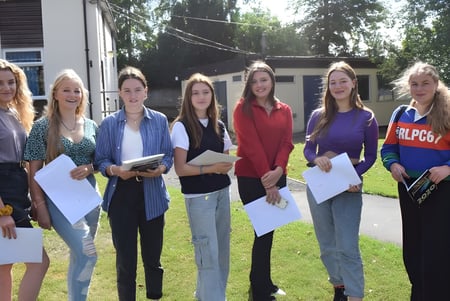 Eine Gruppe Schülerinnen der Rookwood School steht im Freien vor einem Gebäude und hält Papiere in den Händen.