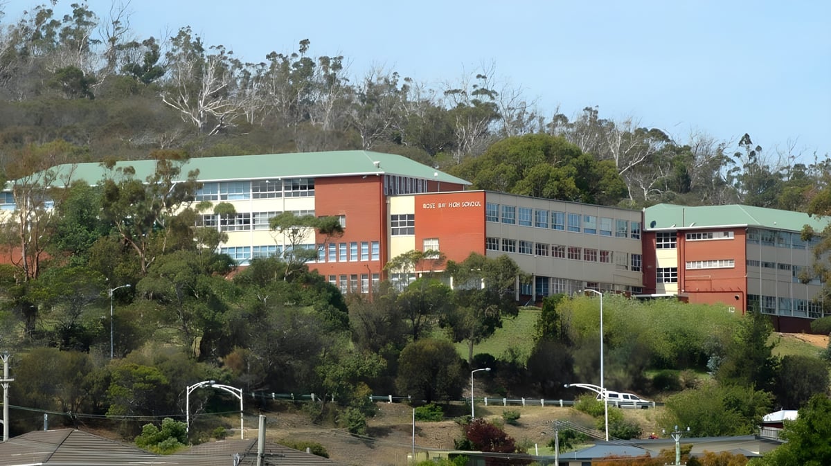 Das mehrstöckige Schulgebäude der Rose Bay High School mit bunten Fassaden ist von grünen Bäumen umgeben.