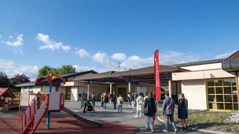 Eine Gruppe Schüler steht vor dem Gebäude der Rose-Des-Vents School im Außenbereich unter blauem Himmel.