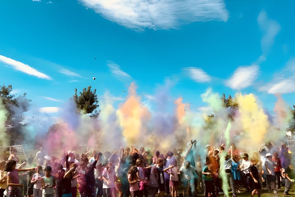 Schüler der Rose-Des-Vents School feiern mit farbigem Pulver vor blauem Himmel.