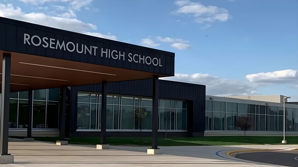 Das moderne Gebäude der Rosemount High School steht vor einem klaren blauen Himmel mit Wolken.