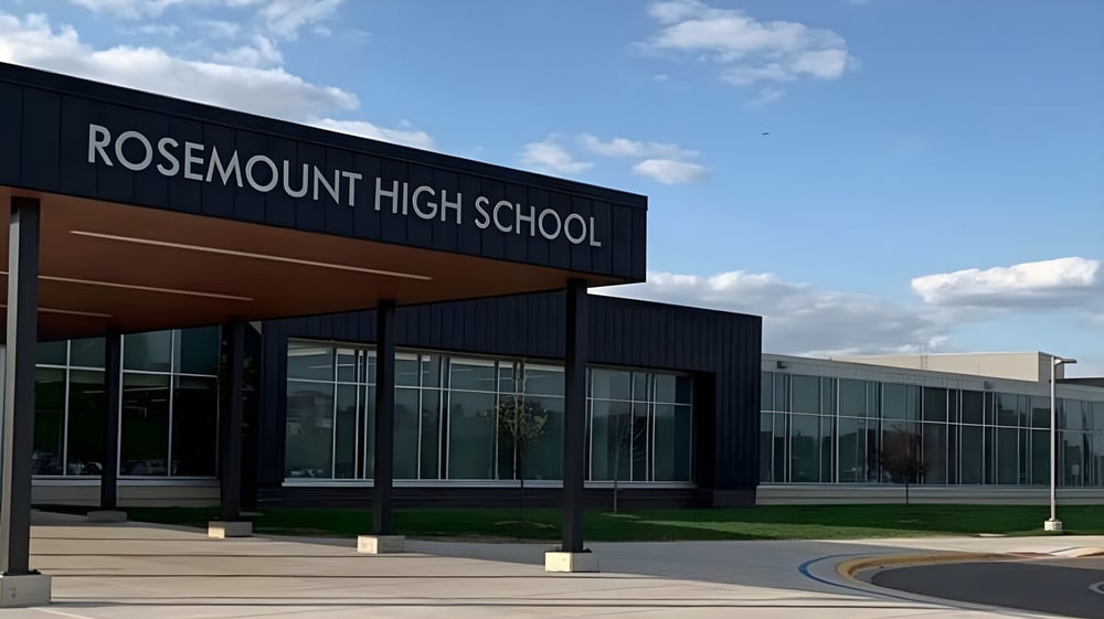 Das moderne Gebäude der Rosemount High School steht vor einem klaren blauen Himmel mit Wolken.