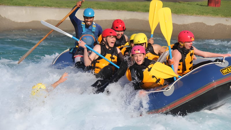 Schüler des Rosmini College fahren mit einem Schlauchboot durch einen reißenden Fluss in einer grünen Landschaft.
