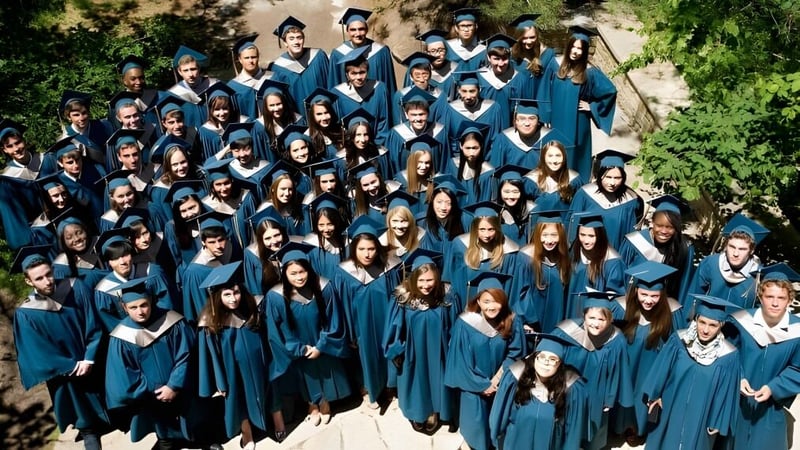 Eine große Gruppe Absolventen der Ross School steht in blauen Talaren und Hüten im Freien vor Bäumen und Grünflächen.