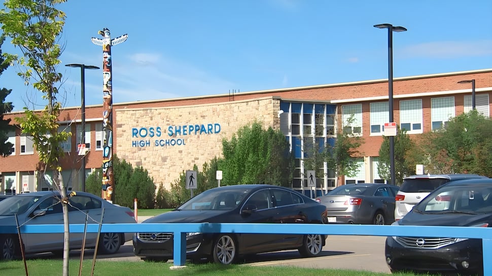 Das Backsteingebäude der Ross Sheppard High School mit dem Schulnamen auf der Fassade und parkenden Autos davor.