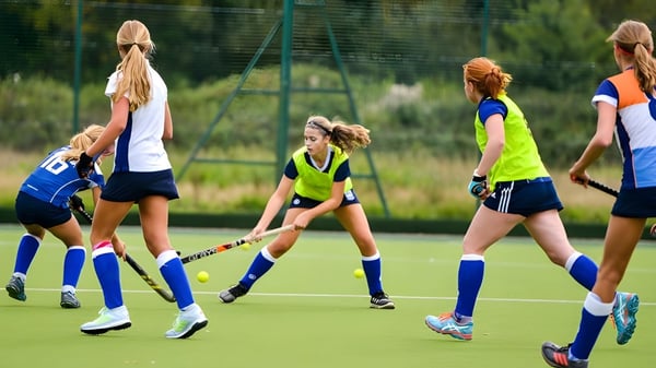 Eine Gruppe junger Schülerinnen spielt Feldhockey auf dem Kunstrasen der Rossall School umgeben von Bäumen.