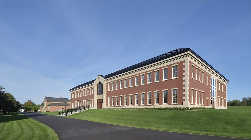 Das mehrstöckige Backsteingebäude der Rothesay Netherwood School steht auf einer Rasenfläche unter klarem Himmel.