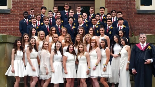 Eine große Gruppe von Schülerinnen und Schülern steht in formeller Kleidung vor einem Backsteingebäude der Rothesay Netherwood School.