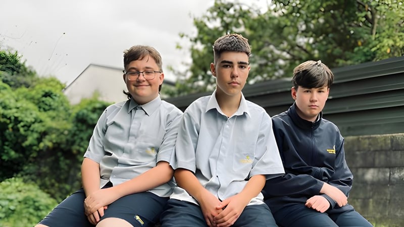 Drei Schüler in Schuluniformen sitzen zusammen im Freien auf dem Gelände der Rotorua Lakes High School vor einem begrünten Hintergrund.