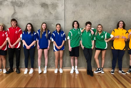 Eine Gruppe junger Sportlerinnen steht in verschiedenen bunten Sportuniformen vor einer Betonwand auf dem Gelände der Roxby Downs Area School.