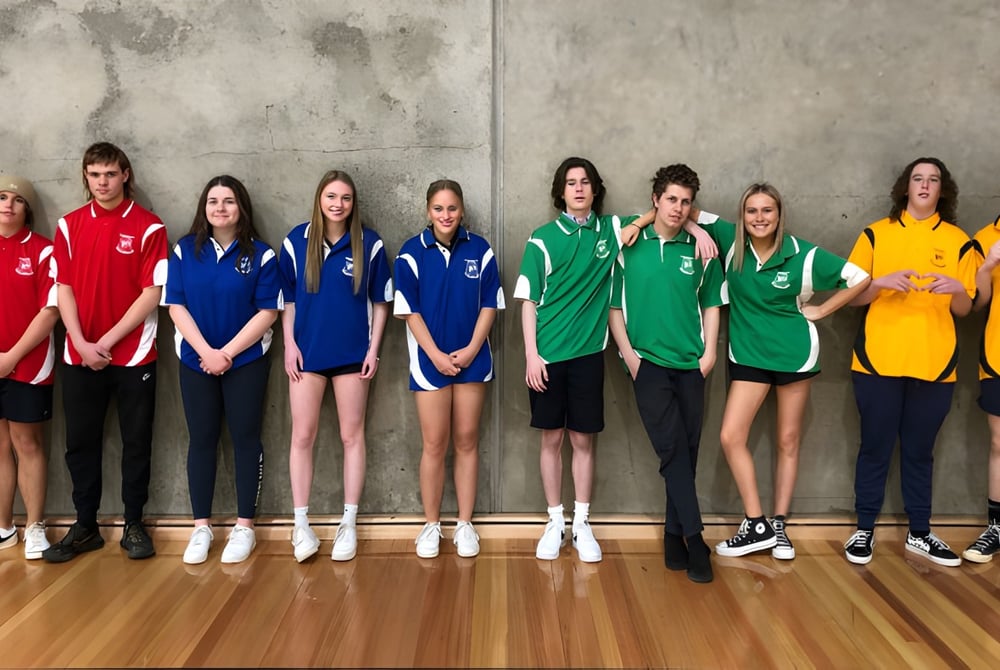 Eine Gruppe junger Sportlerinnen steht in verschiedenen bunten Sportuniformen vor einer Betonwand auf dem Gelände der Roxby Downs Area School.