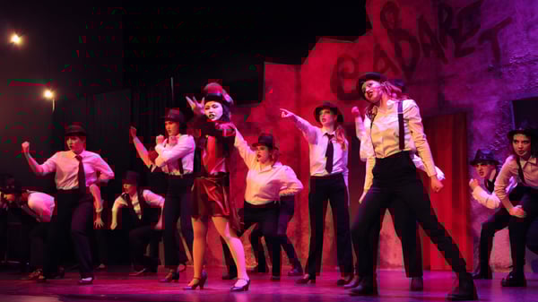 Eine Gruppe von Schülern der Royal Bay Secondary School führt eine lebhafte Tanzaufführung auf einer Bühne mit roter und violetter Beleuchtung auf.