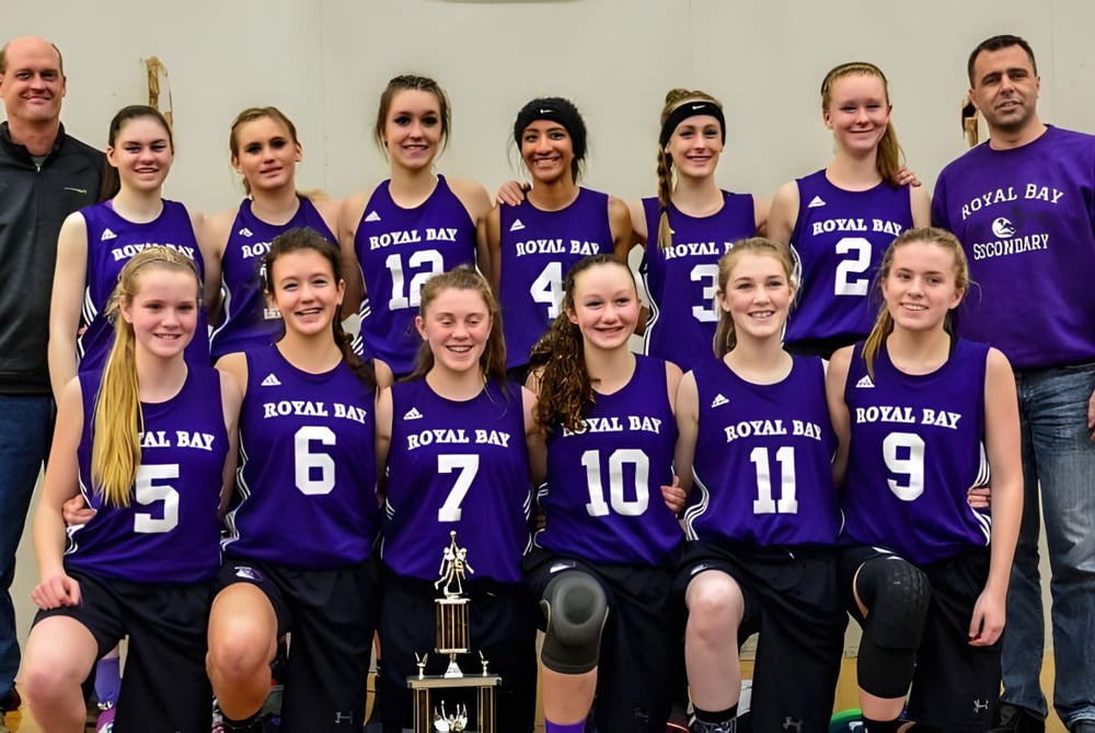 Die Basketballmannschaft der Royal Bay Secondary School steht gemeinsam in einem Raum mit einer Trophäe im Vordergrund.