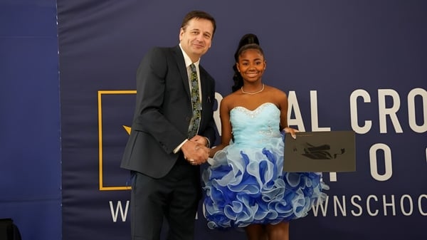 Ein Mann und eine Frau stehen vor einem Banner mit dem Schriftzug der Royal Crown School.