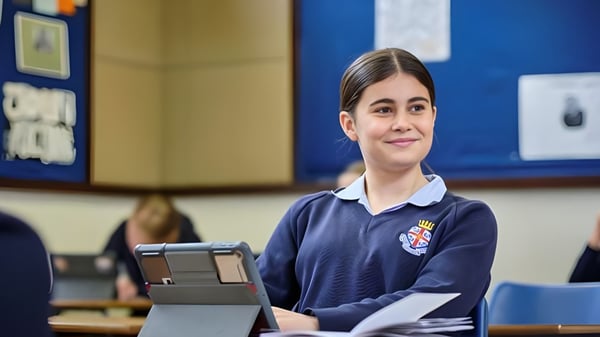 Eine Schülerin der Royal Hospital School steht mit Schuluniform im Klassenzimmer und hält ein Tablet in der Hand.