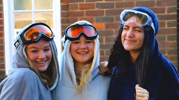Drei Schülerinnen der The Royal Masonic School for Girls stehen lächelnd vor einer Ziegelwand.
