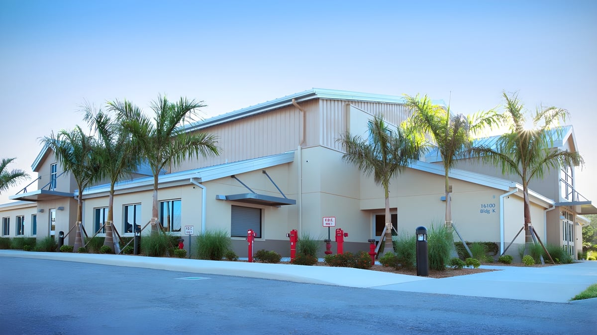 Das moderne zweistöckige Gebäude mit blauem Dach der Royal Palm Academy ist von Palmen umgeben vor klarem Himmel.